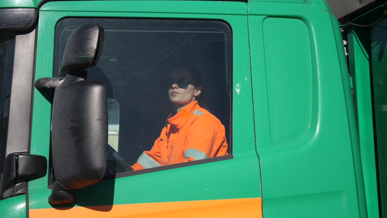 Kvinna sitter bakom ratten i orange varselkläder i ett grönt Ragn-Sells fordon